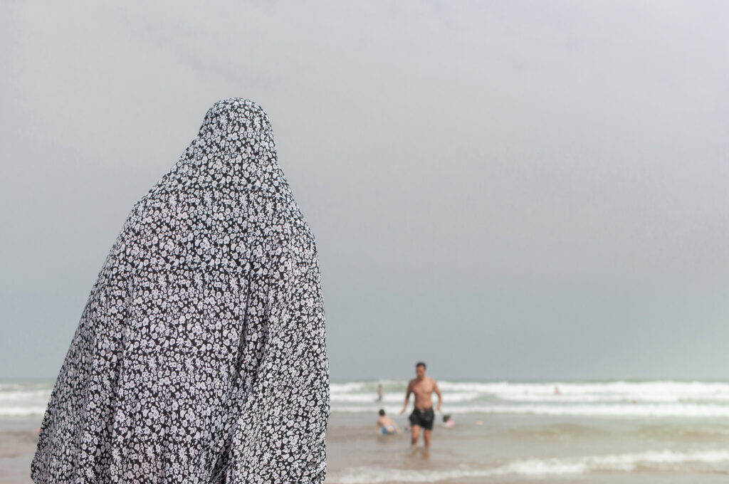 Femme voilée observant son fils et son mari se baigner dans la mer. Casablanca, août 2016 © Karen Assayag